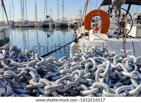 Anchor chain pile closeup view, Heavy industrial chain on the harbor deck, blur cruise yachts moored in a marina background