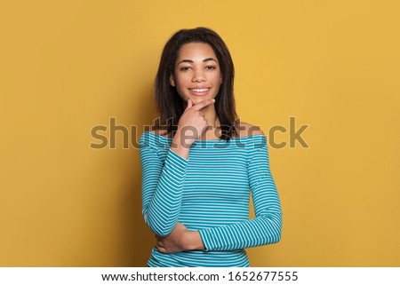 Cute smart mixed race ethnicity black woman in blue shirt thinking on colorful yellow background
