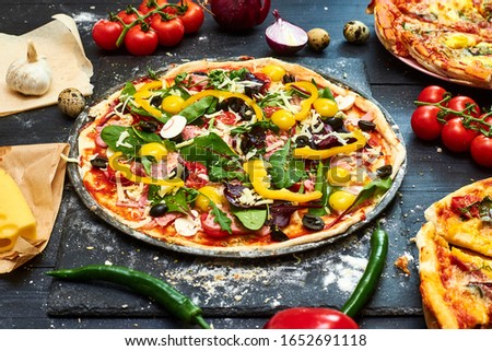 Raw pizza with mozzarella cheese, meat, tomatoes, mushrooms, peppers, herbs on a dark wooden background. Cooking delicious italian pizza.