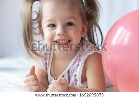 Young children lie on their stomachs and watch cartoons. Beautiful kids lie on the bed with colorful ballons. Party time. Celebration, childhood birthday, holiday concept 