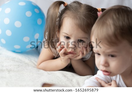 Young children lie on their stomachs and watch cartoons. Beautiful kids lie on the bed with colorful ballons. Party time. Celebration, childhood birthday, holiday concept 