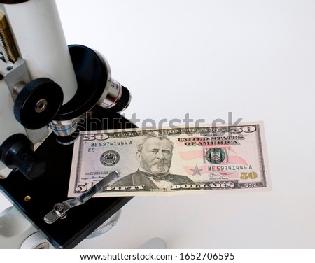 50 dollars lies on a microscope stage. The corner of the bill is clamped in the clip