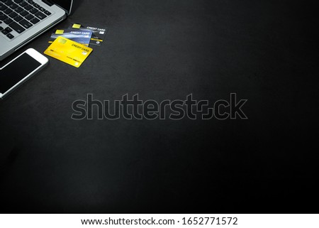 Laptop, white mobile phone and credit cards against empty dark background