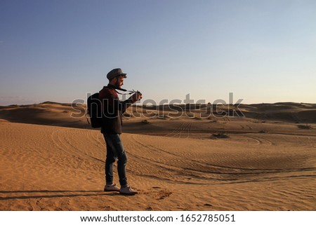 Traveller man with hat and sunglasses taking pictures in the desert during sunset