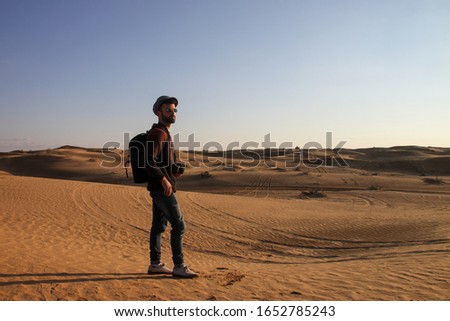 Explorer man with hat and backpack taking pictures in the desert