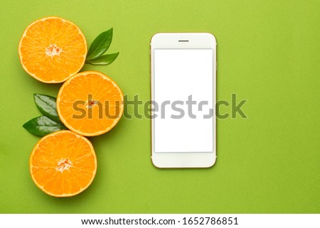 Mobile phone and tangerine on an green background, fruit flatlay, summer minimal compositon