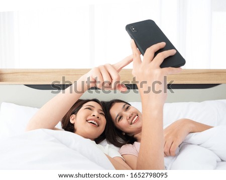 Asian young cute girl use mobile for watching movie series, video channel, reading social media comment feed or selfie photo teenage lifestyle while lie down on white bed in bedroom's friend at home