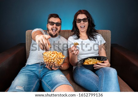 A man and a woman, a family watching a movie or a series in 3D glasses, a blue background. The concept of a cinema, films, emotions, surprise, leisure, streaming platforms