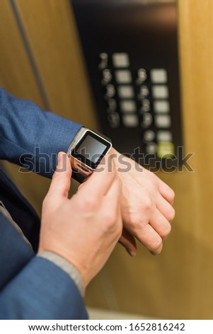 Man with smartwatch on his hand with elevator control panel in the background.