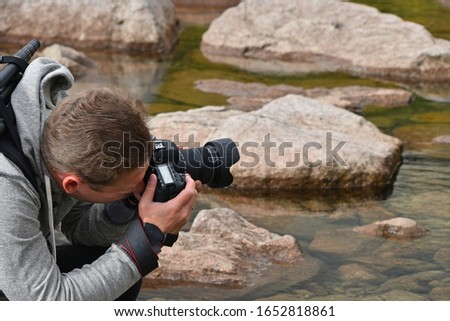 One young adult tourist man photographer with backpack taking pictures of mountain lake on foggy weather day, high angle side view
