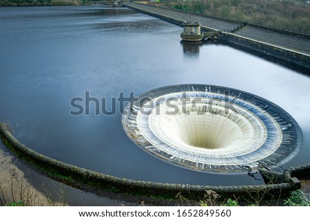 Ladybower Reservoir is the lowest of three reservoirs in the Upper Derwent . Bellmouth overflows (locally named the "plugholes") at the side of the wall. Royalty-Free Stock Photo #1652849560