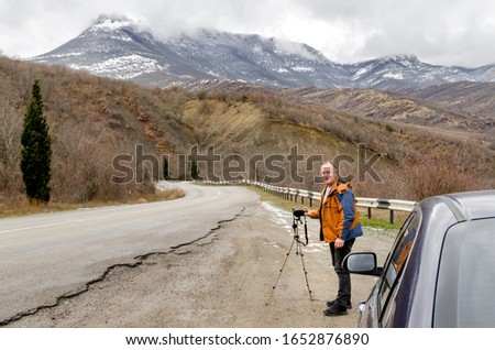 cheerful photographer stopped on a mountain road to take a shot of a beautiful landscape