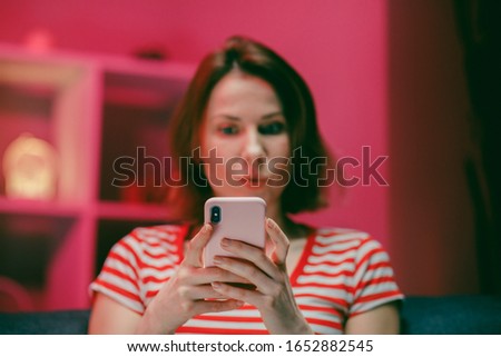 Young Woman Holding Smart Phone Looking at Cellphone Screen Laughing Enjoying Using Mobile Apps for Shopping. Having Fun Playing Games Chatting in Social Media Sit on Couch at Home
