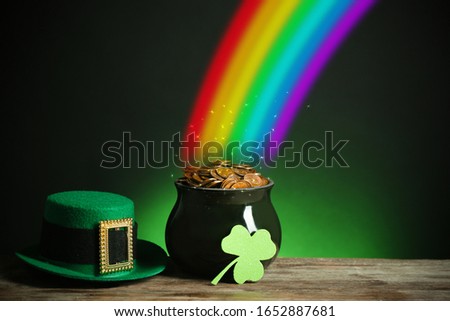 Pot with gold coins, hat and clover on wooden table against dark background, space for text. St. Patrick's Day