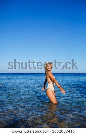 girl in a light hat and a beige swimsuit splashes in the blue water of the Red Sea