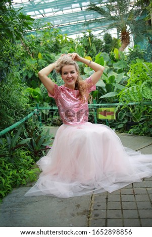 beautiful girl with long white hair in pink top and pink light fanin skirt enjoys nature in the garden