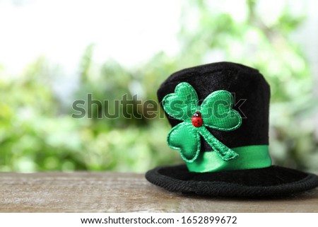 Black leprechaun hat with clover leaf on wooden table, space for text. St Patrick's Day celebration
