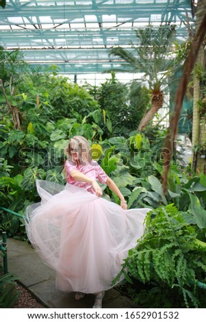 beautiful girl with long white hair in pink top and pink light fanin skirt enjoys nature in the garden