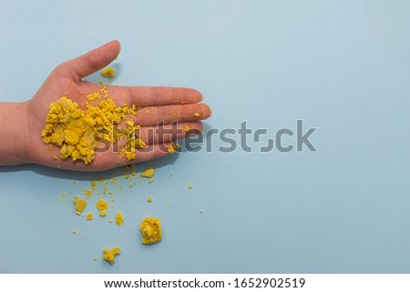 Crumbled macaroon cookie on female palm on blue flat background. Picture with copy space