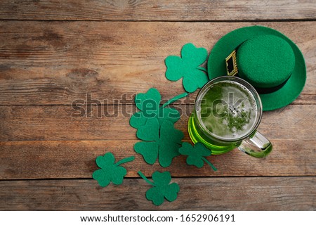 Green beer, hat and clover leaves on wooden table, flat lay with space for text. St. Patrick's Day celebration