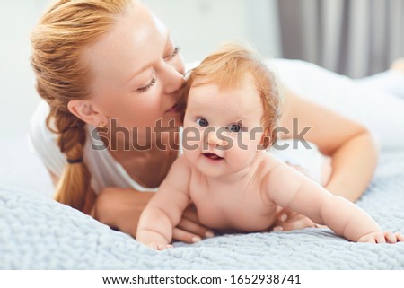 Mother kisses the baby lying on the bed