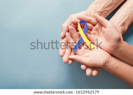 Adult and child hands holding blue and yellow ribbon shaped paper, Down syndrome awareness , World down syndrome day Royalty-Free Stock Photo #1652962579