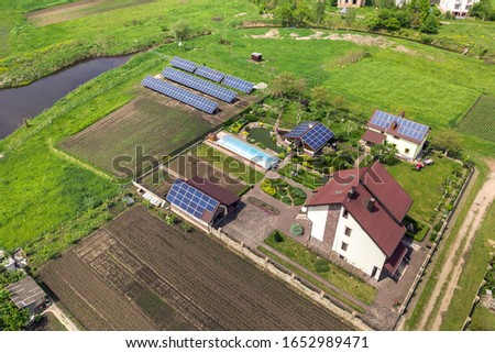 Aerial view of a private house in summer with blue solar photo voltaic panels on roof top and in the yard.