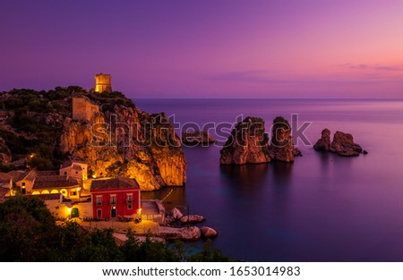 Dawn scene of lit up old tuna factory (Tonnara di Scopello), ancient tower (Torre Doria) and coastal rock stacks (faraglioni), Sicily, Italy. 