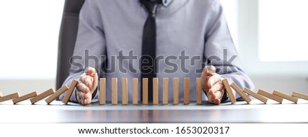 business man blocks falling blocks with his hands to prevent domino effect