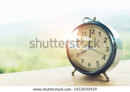 Selective focus of alarm clock on table with nature bokeh mountain background. Time in life concept