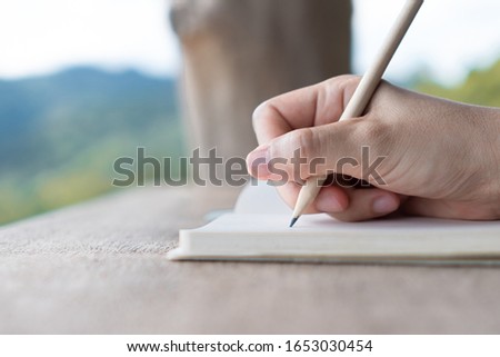 Woman hand writing down in small white memo notebook for take a note not to forget or to do list plan for future.