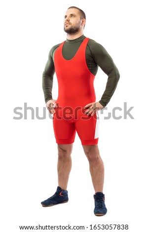 A strong strong young man in a sports red tights is standing with his hands on his sides, looking confidently forward on a white isolated background. 
Greco-Roman wrestler for sports design.