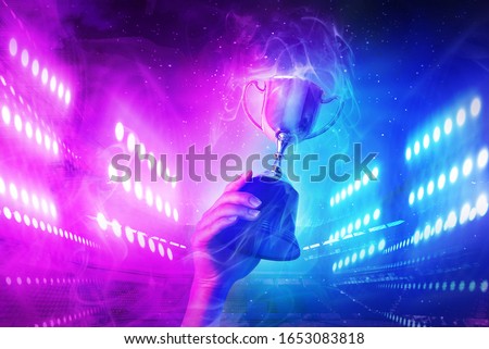 Trophy with smoke effect holding on hand and background blue and violet light for e-sport winner event.   