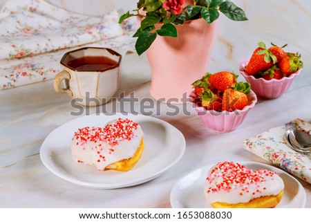 Party table with heart shaped donuts, strawberry, tea and vase with rose. Valentine Day concept.