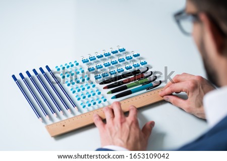 A Person's Hand Arranging Pencils And Multi Colored Pushpins In A Row On White Background Royalty-Free Stock Photo #1653109042