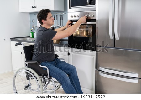 Disabled Man Using Microwave Oven For Baking In Kitchen Royalty-Free Stock Photo #1653112522