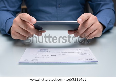 Man Taking Photo Of Cheque To Make Remote Deposit In Bank Royalty-Free Stock Photo #1653113482