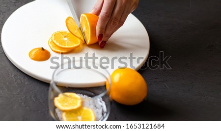 Dark moody. Food black background. On a white stone board in the hands of a girl, a knife cuts a lemon. Slices of lemon are piled in a glass jar and sprinkled with sugar. In the foreground is a whole