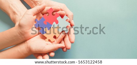 Adult and chiild hands holding jigsaw puzzle shape, Autism awareness, Autism spectrum family support concept, World Autism Awareness Day