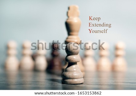 The concept of success in business. In the foreground is a pawn, just behind it is a Queen figure. In the background, pawns in a row. The inscription on the right: "keep extending yourself"