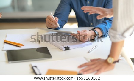 Close up view of two businessman briefing on their work with tablet and document file on white desk in simple meeting room