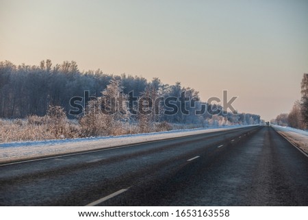 Asphalt road. Auto track. Large snowdrifts of white snow. Winter landscape. Sunny weather in the cold. Trees in the snow. Blue sky. Forest and grass in hoarfrost.