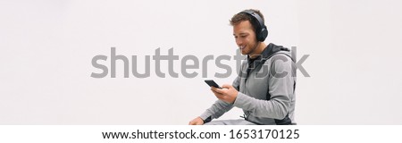 Man listening to music mobile phone app wearing headphones sitting at home white wall background panoramic. Happy guy active lifestyle sport athlete using smartphone at gym outside panorama banner.