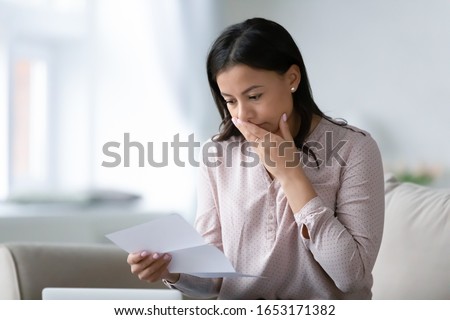 Distressed African American young woman sit on couch at home read bad negative news in paper correspondence, unhappy biracial female stressed consider unpleasant message in postal letter Royalty-Free Stock Photo #1653171382
