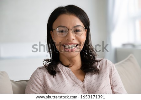 Headshot portrait of smiling African American young woman in glasses sit pose on couch in living room, profile picture of happy biracial confident female in spectacles relax on sofa at home laughing