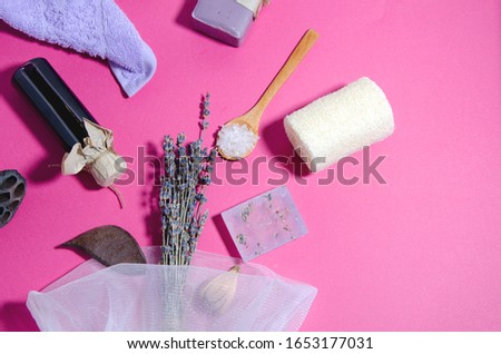 SPA accessories lie on a pink background. Purple towel, lavender oil and soap, salt, loofah washcloth, bag with a bouquet of lavender. Horizontal image, flat lay