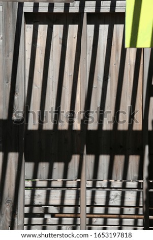 Close up outdoor perspective view of many shadows of a modern wooden structure reflected on the floor. Abstract design with pattern of dark parallel lines and geometric shapes. Architectural picture. 