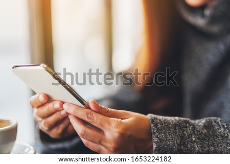 Closeup image of a woman holding and using mobile phone with coffee cup on the table in cafe
