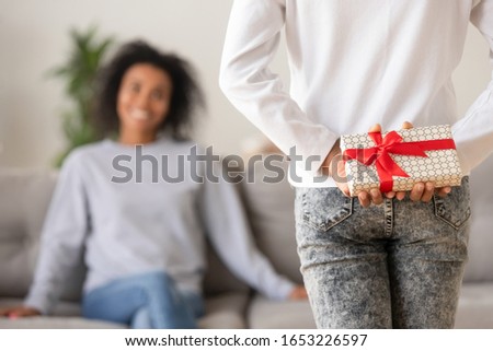 Rear view of teen african american kid daughter holding gift behind back prepare present for mothers day congratulate happy young mom with birthday, child girl hiding box make surprise to mum at home
