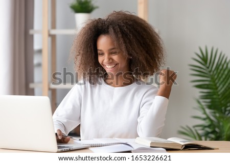 Excited happy overjoyed african american teen school girl student winner celebrating victory reading admission email with good exam test results received great news online looking at laptop computer. Royalty-Free Stock Photo #1653226621